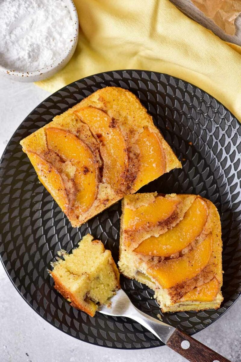 Top view of two pieces of peach upside down cake on a black plate.
