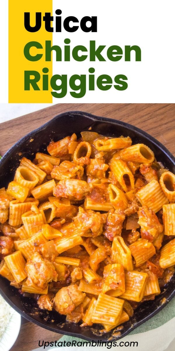 A skillet filled with cheesy Utica chicken riggies, featuring tender pasta, chicken, and savory red sauce, sits on a wooden table. The text reads "Utica Chicken Riggies.