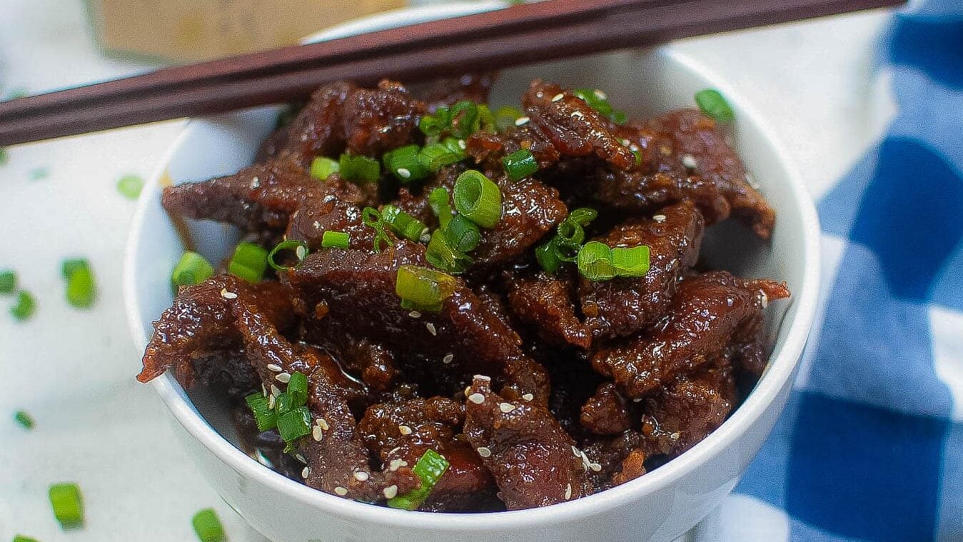 Closeup of crispy beef in a bowl with green onions and sesame seeds.