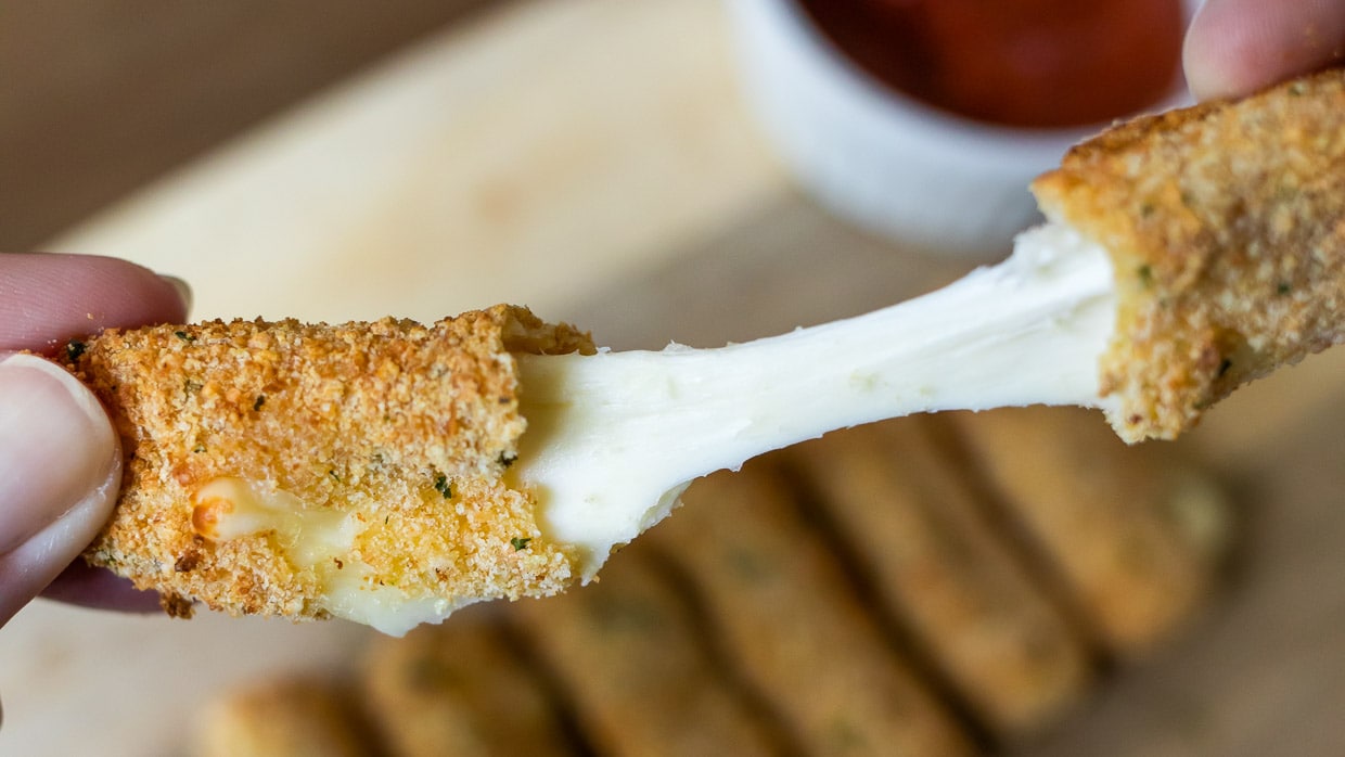 Pulling apart an air fryer mozzarella stick to show the gooey cheese inside.