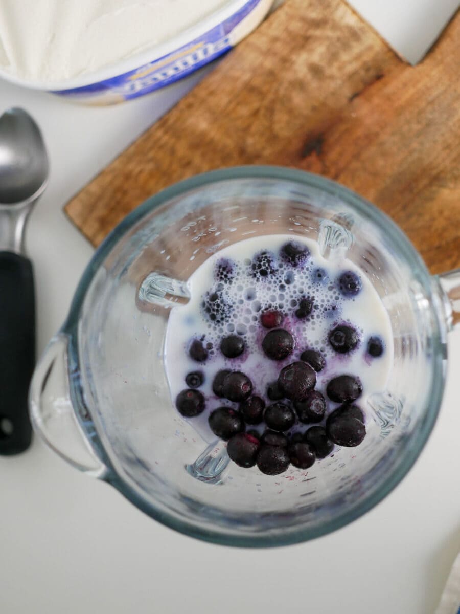 Adding the milk to the blender for a blueberry milkshake.