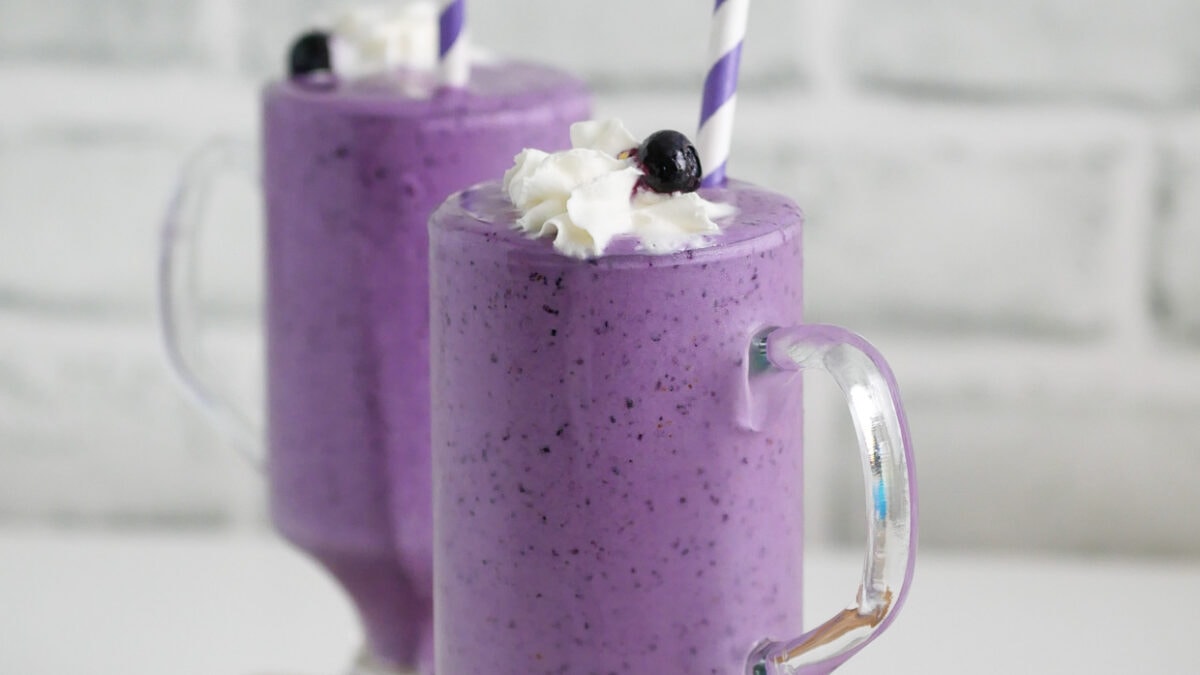 Blueberry milkshakes with whipped cream and a straw.