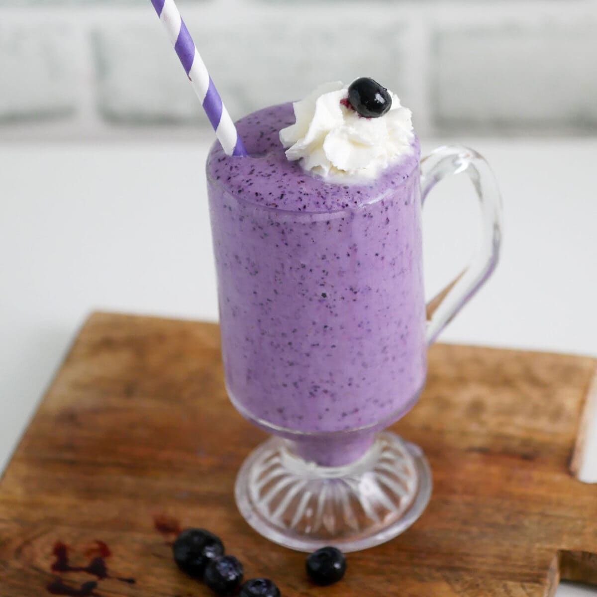 Blueberry milkshake in a glass topped with whipped cream and a purple straw.
