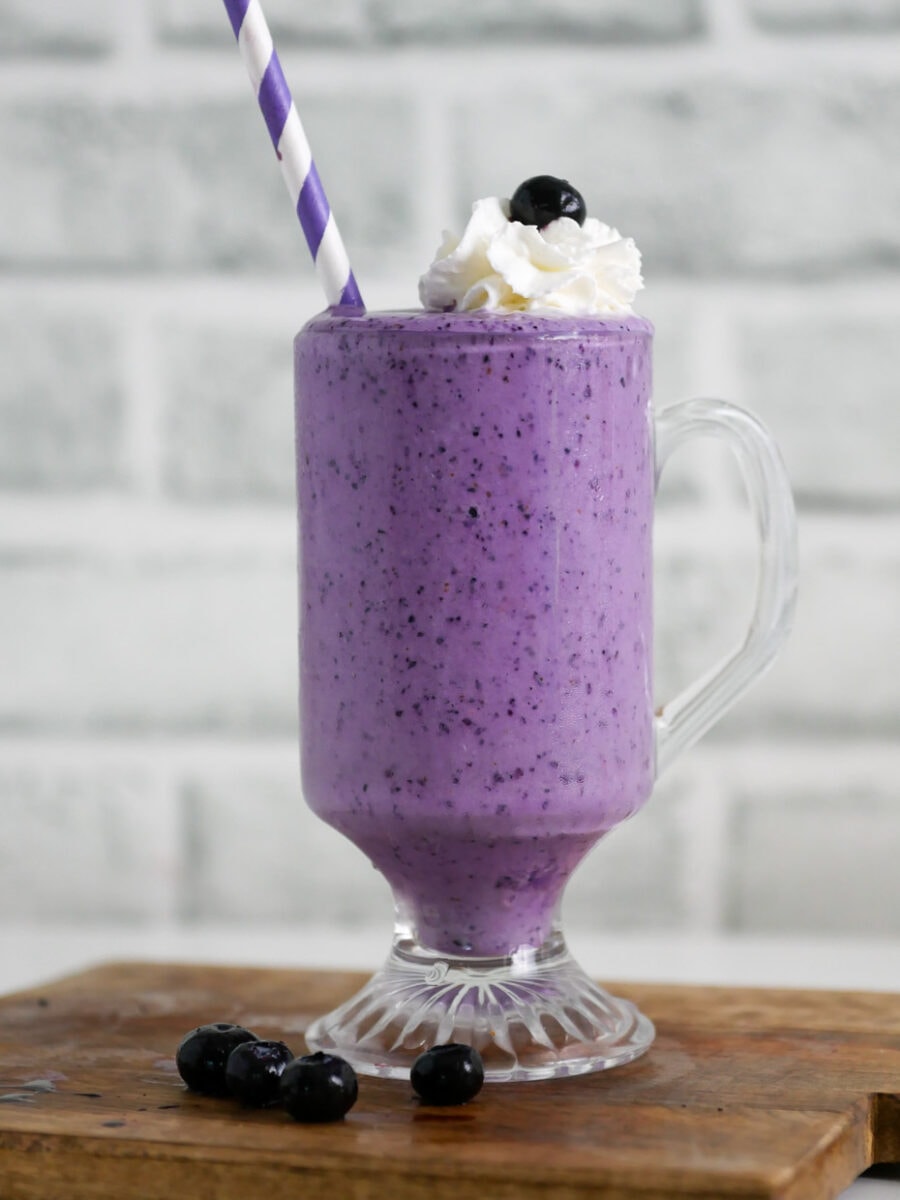Blueberry milkshake on a cutting board with whipped cream and a straw.
