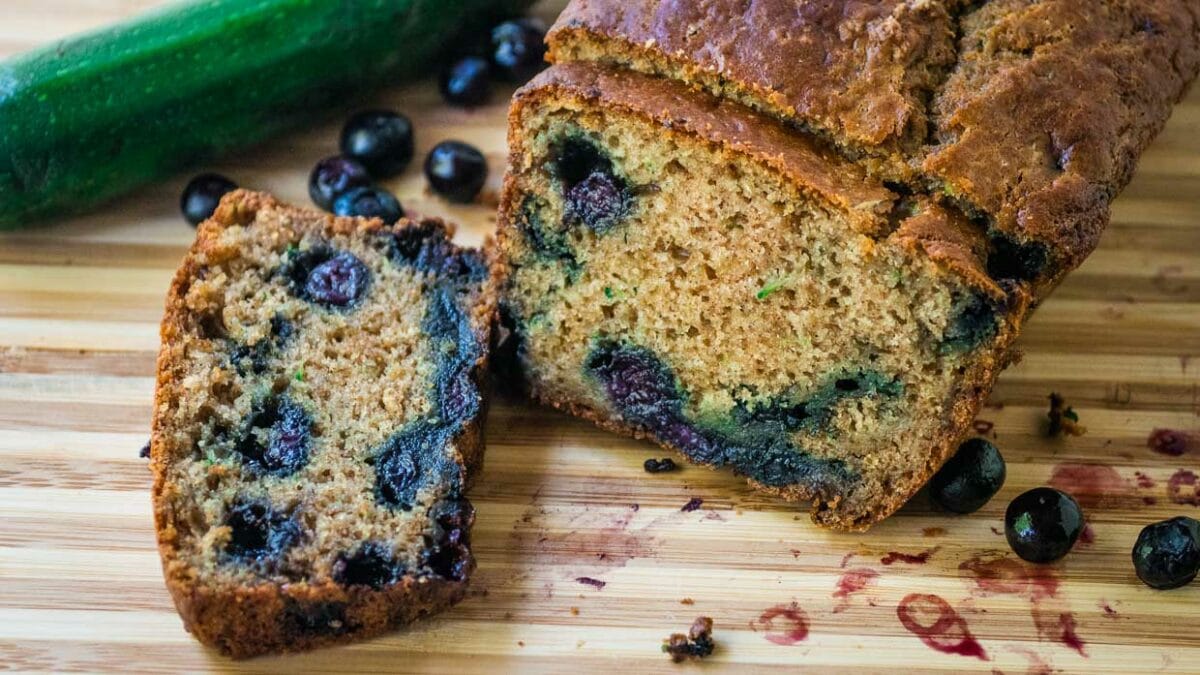 Loaf of zucchini bread with blueberries sliced on a cutting board.