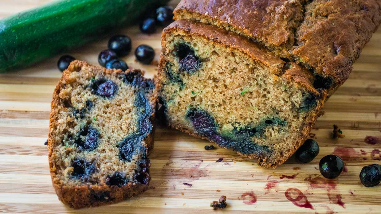 Loaf of zucchini bread sliced to show the blueberries inside.
