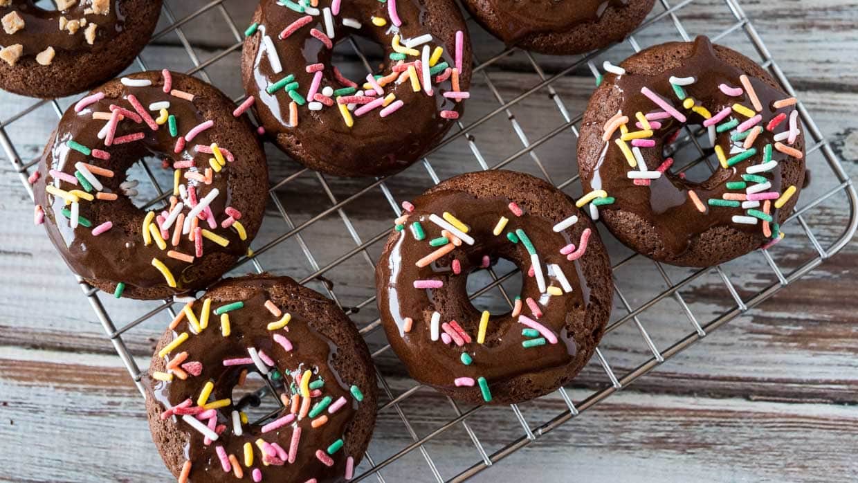 Chocolate cake mix donuts with colorful sprinkles on a baking rack.