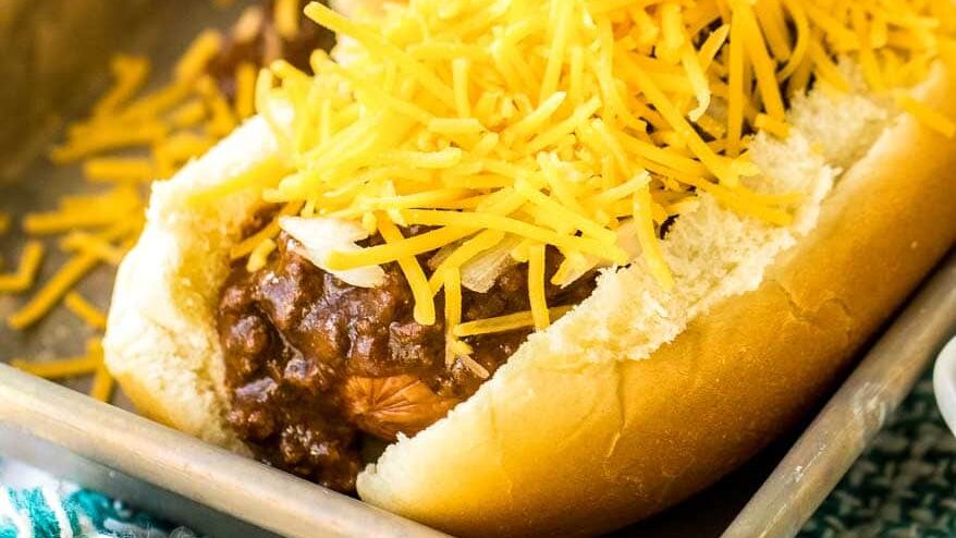 topping a hot dog with Chili and cheese.