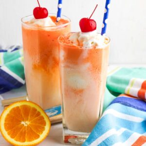 Two creamsicle floats in tall glasses with blue straws.