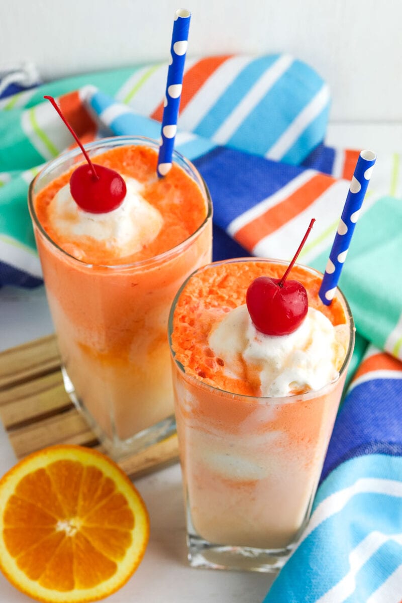 Two glasses of orange float topped with whipped cream.