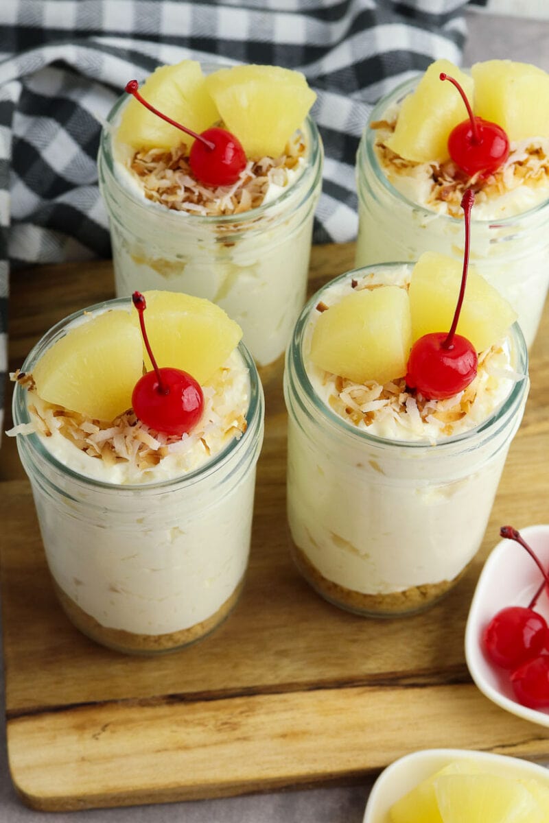 Top view of pina colada cheesecake in mason jars garnished with pineapple and a cherry.
