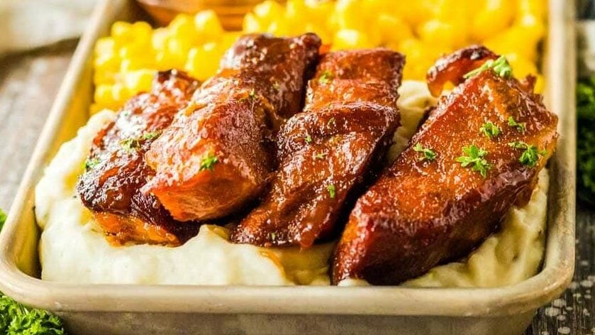 Slow cooker country style ribs on a tray on top of mashed potatoes with corn.