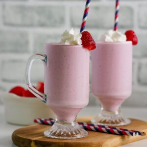 Banana strawberry milkshake with whipped cream, a berry and a straw.