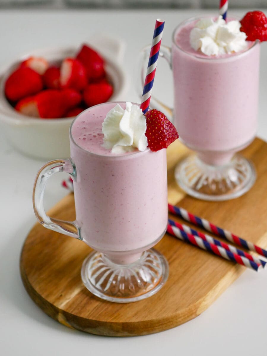 Two glasses of banana strawberry shake with whipped cream and a strawberry.