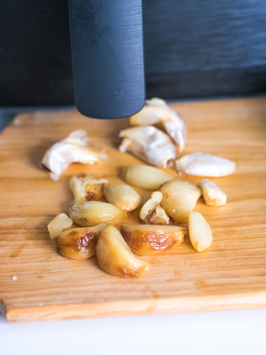 Roasted garlic cloves in front of air fryer.