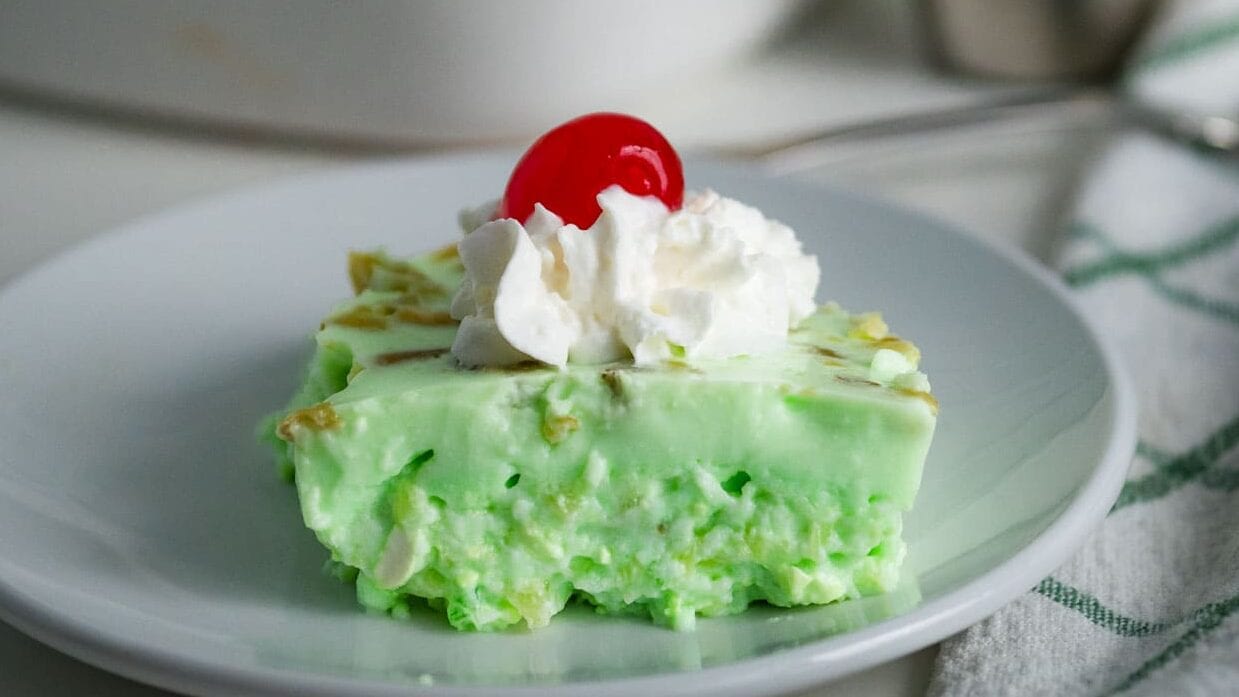 Piece of lime jello salad topped with whipped cream and a cherry.