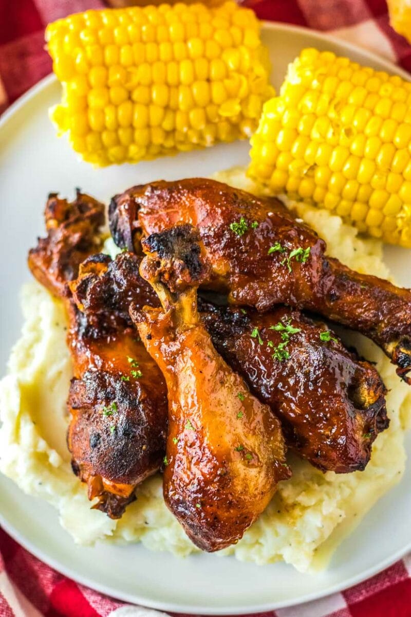 BBQ chicken legs on a plate with corn and mashed potatoes.