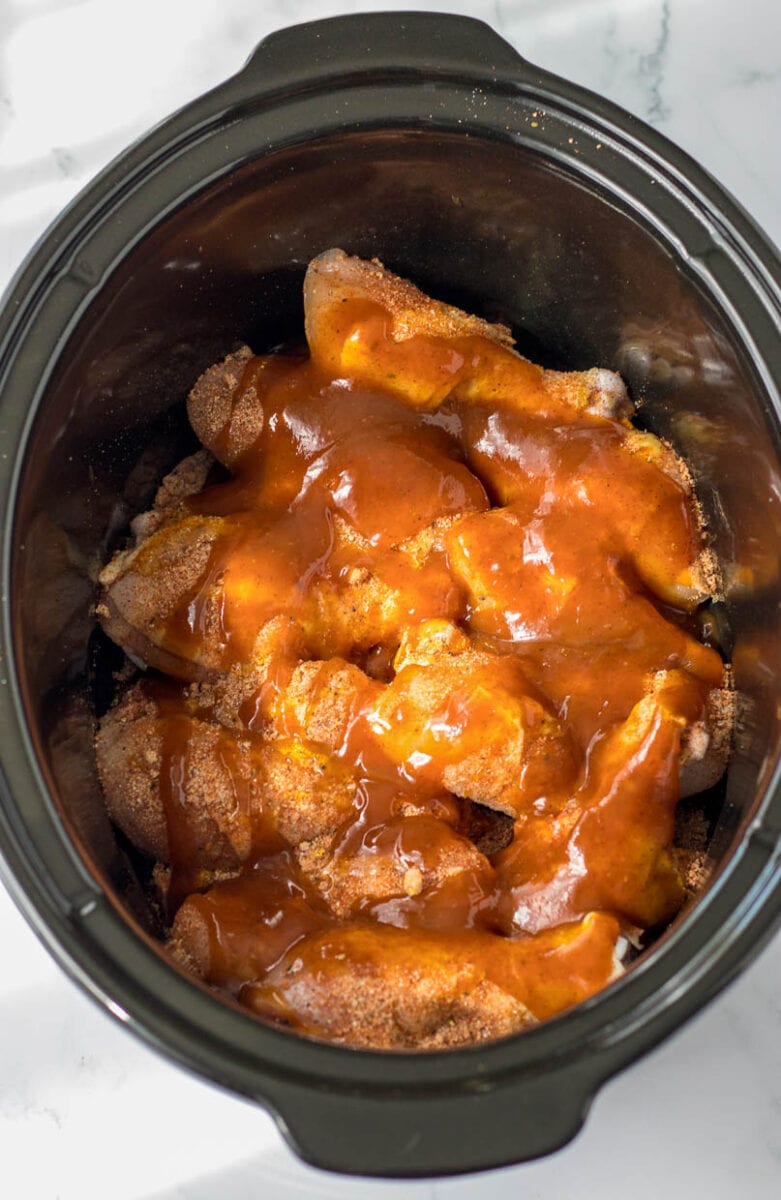 Adding the BBQ sauce to the chicken legs in a slow cooker.
