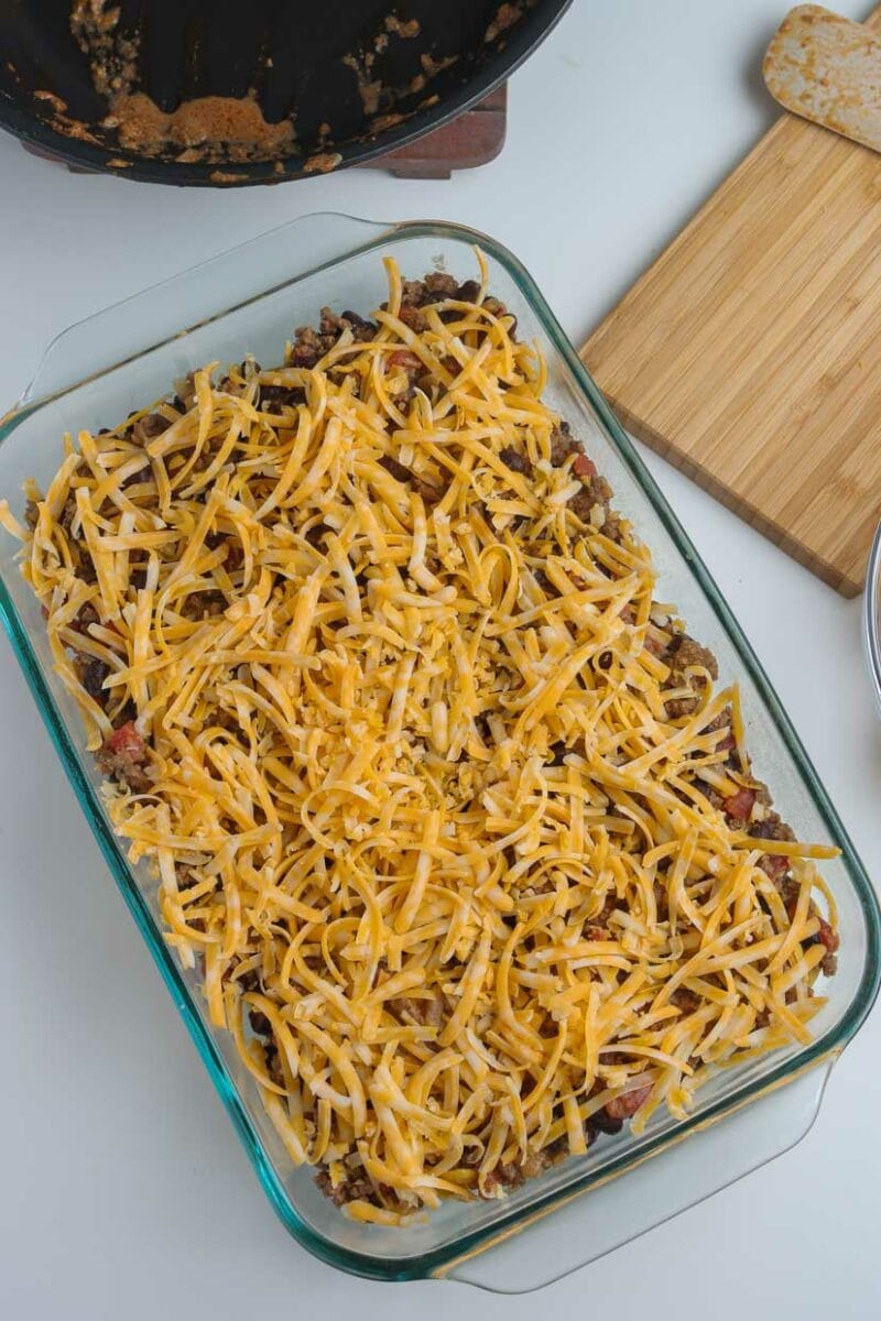 Adding the cheese to the walking taco casserole.