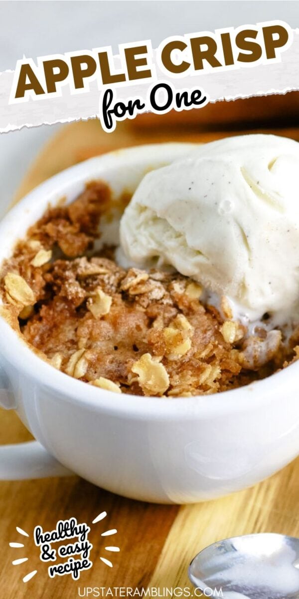 A warm apple crisp in a mug, topped with a scoop of vanilla ice cream, sits on a wooden surface with text reading "Apple Crisp for One.