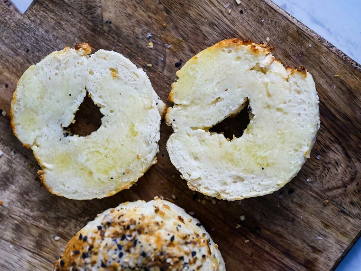 Two bagels with sesame seeds on a cutting board.