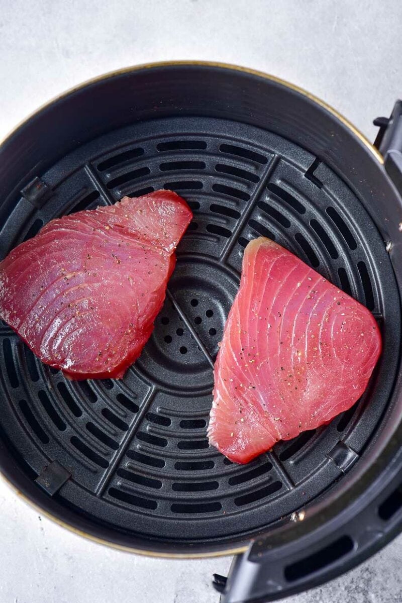 Rqw ahi tuna steaks in the basket of an air fryer.
