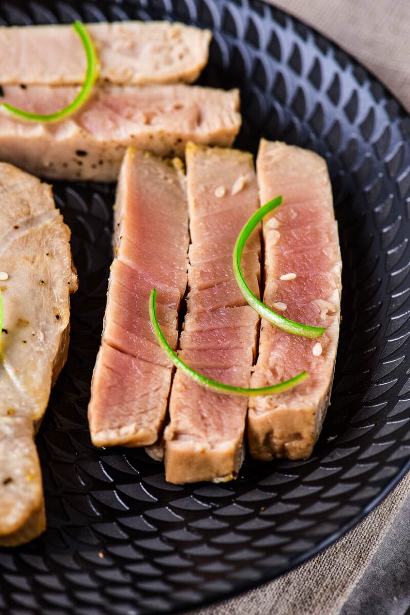 Slice tuna steak on a black plate.