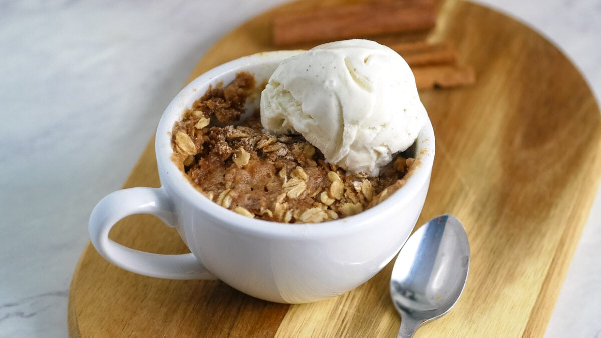 A mug with apple crisp and ice cream and a scoop of ice cream.