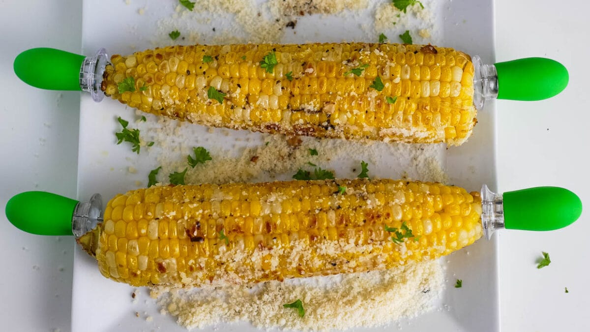 Two ears of garlic parmesan corn on a white plate.