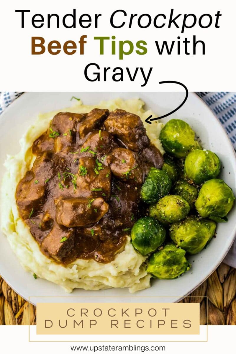 A plate of slow cooker beef tips with gravy served over mashed potatoes, accompanied by Brussels sprouts and garnished with fresh herbs.