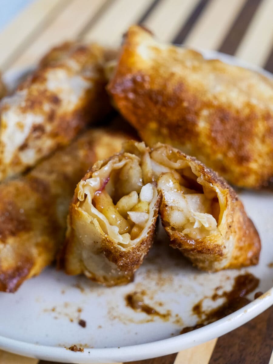 Air fryer apple pie egg rolls cut in half and stood on a plate to show the insides.