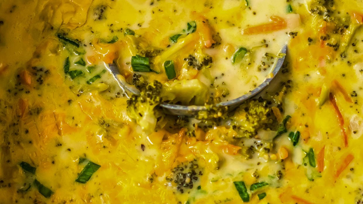 A bowl of broccoli cheddar soup with broccoli and carrots.