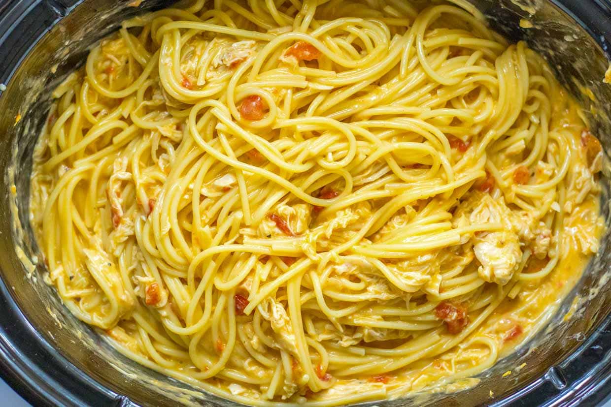 A crock pot filled with spaghetti and chicken.