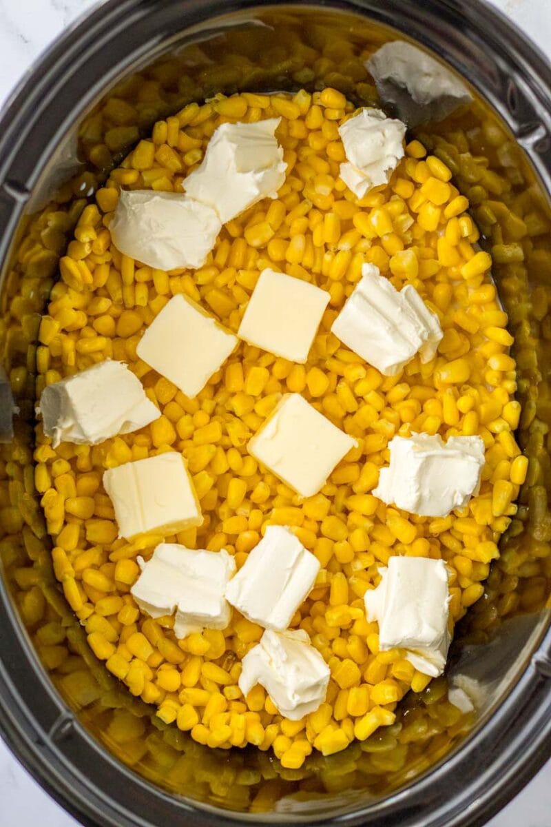 Adding the butter and sugar to the creamed corn in the slow cooker.