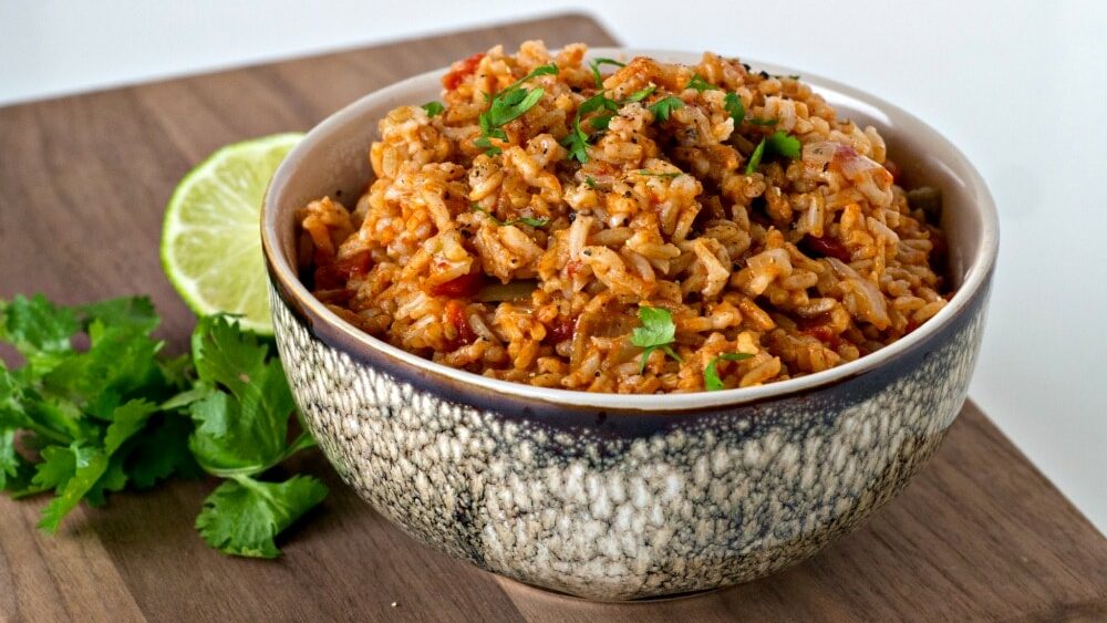 Mexican rice in a bowl on a wooden cutting board.