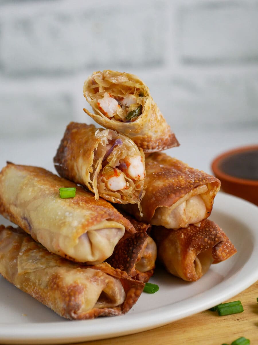 Big stack of egg rolls on a plate with sauce.