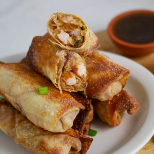 Stack of egg rolls on a plate with one cut in half.