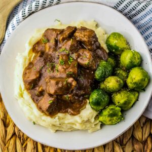 A plate of beef tips with mashed potatoes and brussels sprouts.
