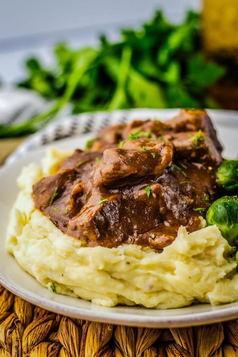 Beef tips on a plate with mashed potatoes and brussels sprouts.