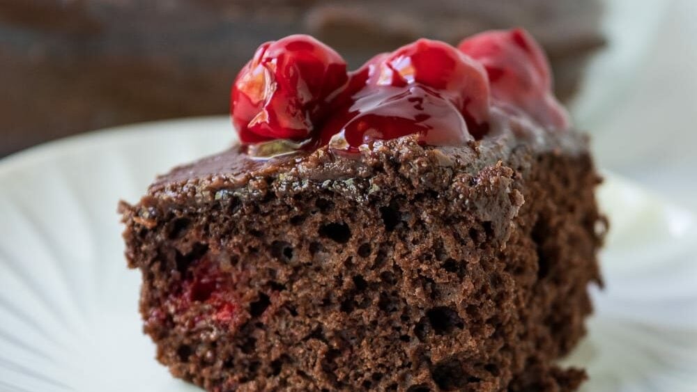 slice of chocolate cherry cake on a plate with cherries on top