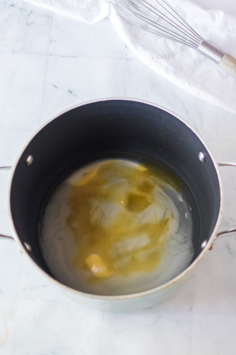 A pan with eggs in it and a whisk next to it.