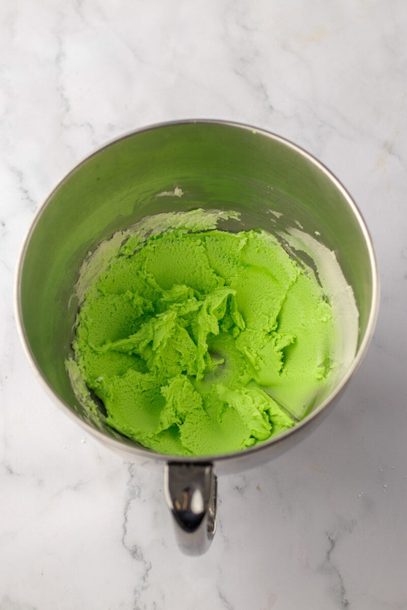 Green icing in a bowl on a marble countertop.