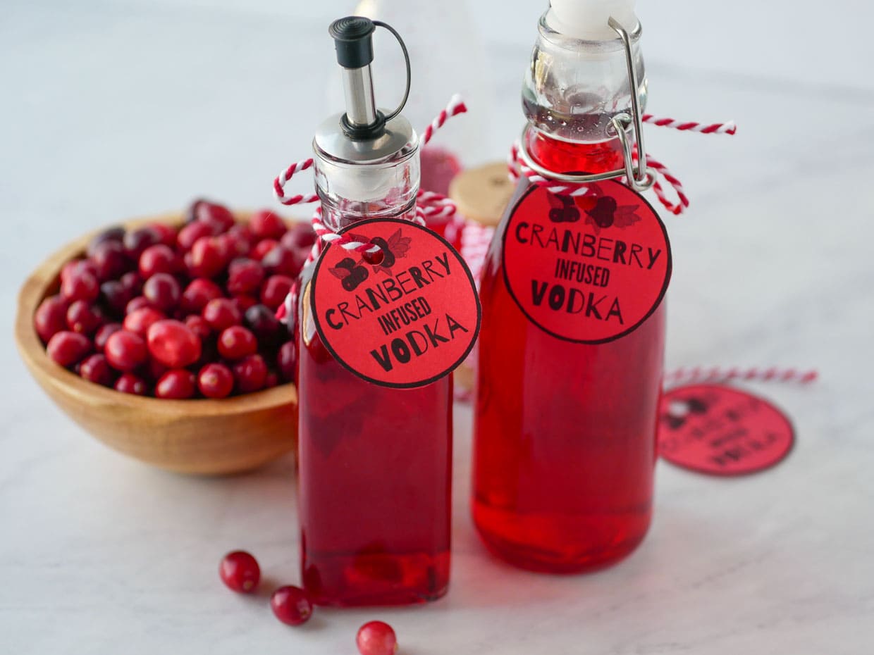 Two bottles of cranberry vodka and cranberries on a table.