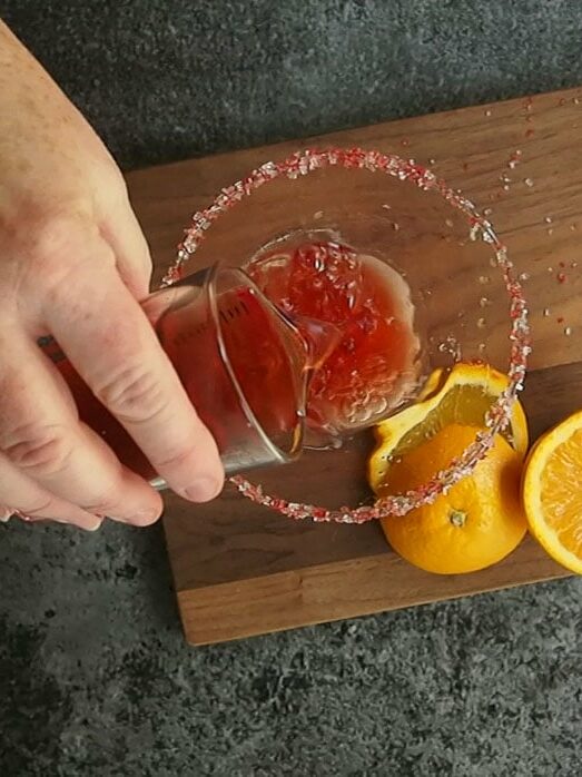 A person pouring orange juice into a martini glass.