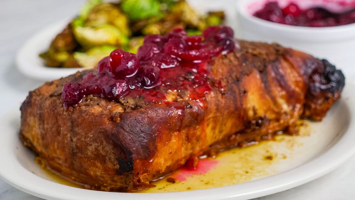 A roast with cranberry sauce and brussels sprouts on a plate.