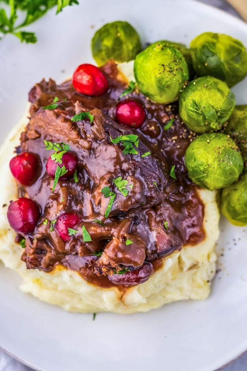 A plate of mashed potatoes and beef with cranberries and brussels sprouts.