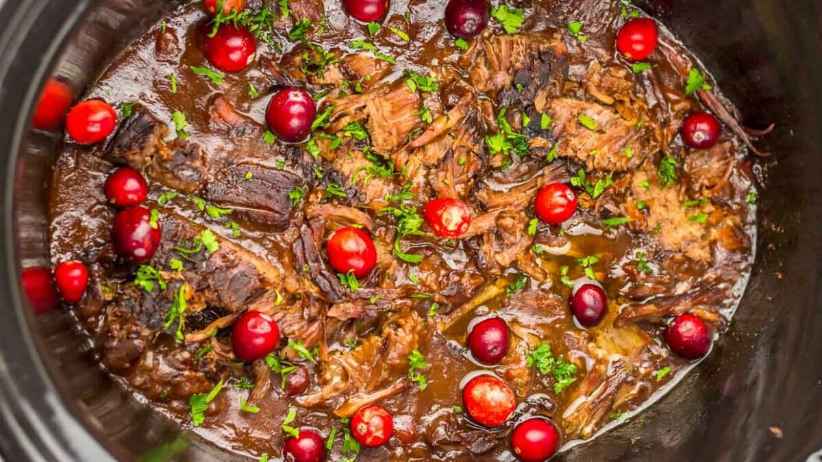 A slow cooker filled with beef and cranberries.