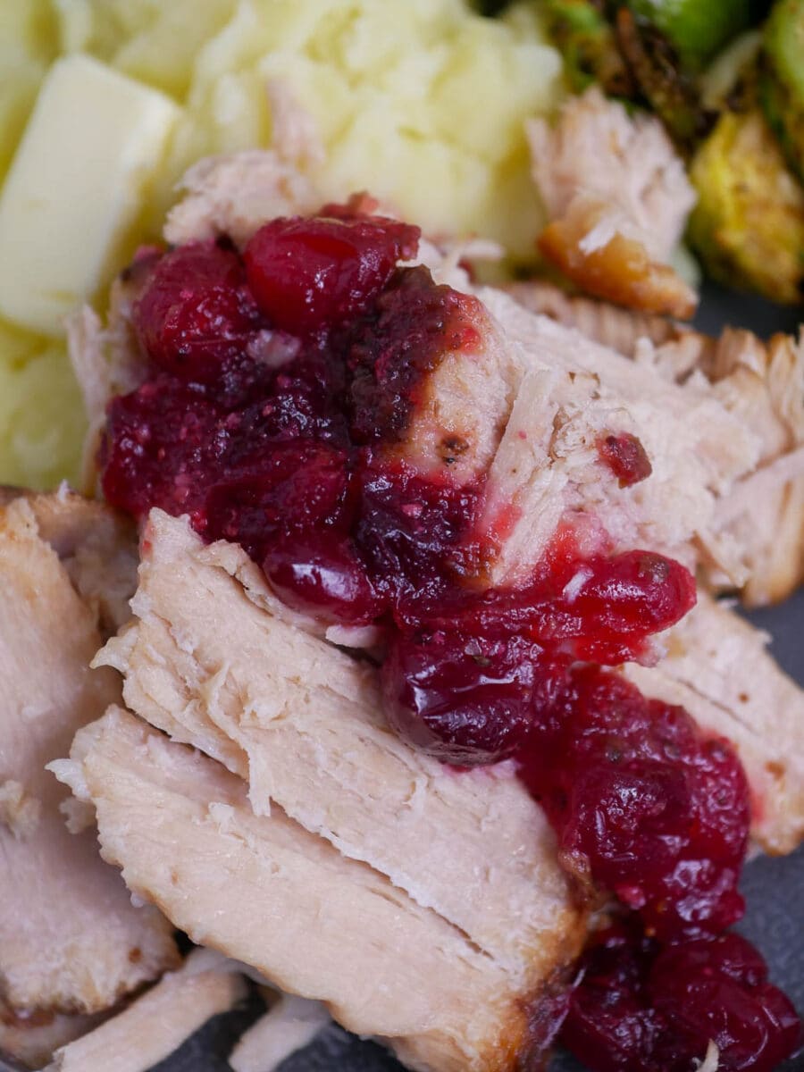 A plate of roasted turkey with cranberry sauce and brussels sprouts.