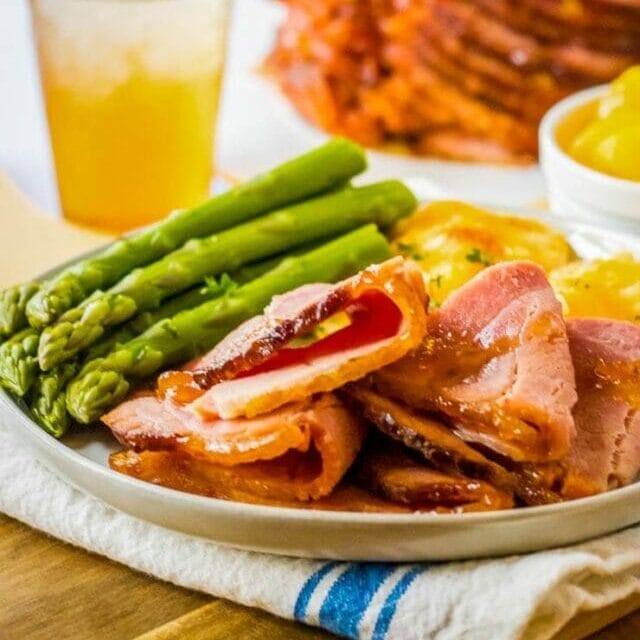plate of ham and asparagus with slow cooker spiral ham in background.