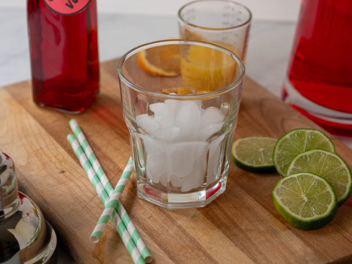 A glass with ice and a straw on a cutting board.
